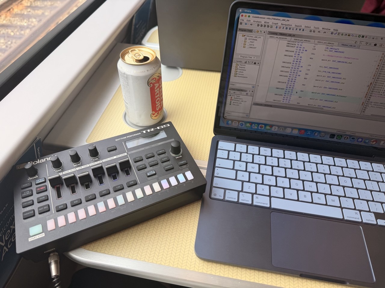 TR-6S powered on on Amtrak Acela, Macbook Neo with Ghidra open, Stella Artois Beer in background